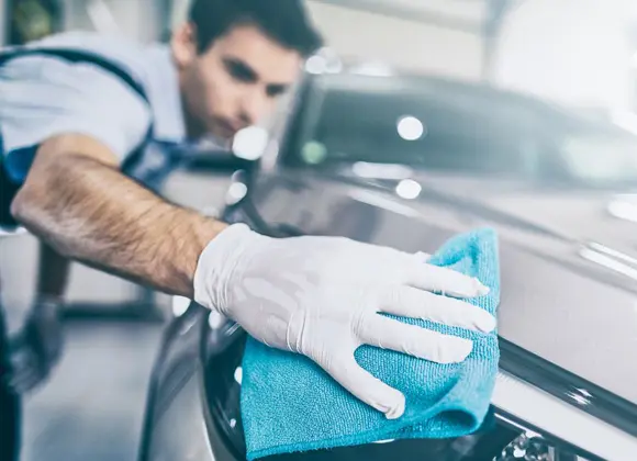 Auto body technician cleaning vehicle surface with microfiber cloth, emphasizing quality repair and restoration services at Buffalo Customs & Collision in San Antonio.